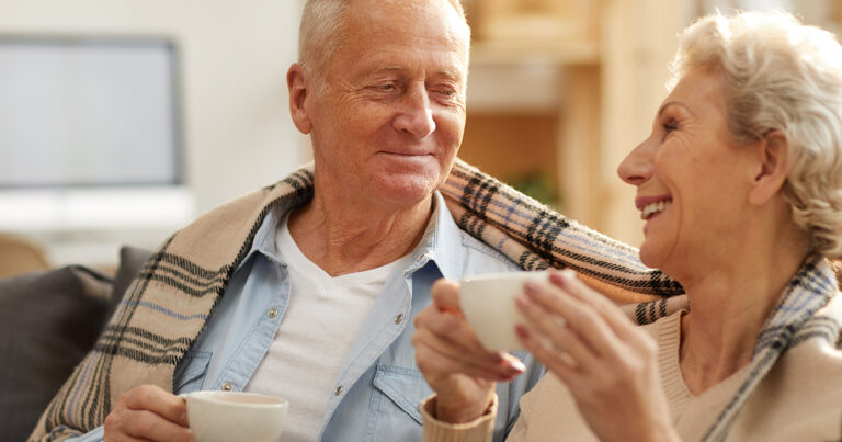 Senior couple sitting together on couch drinking from a mug